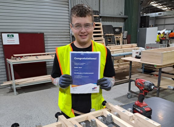 Eddie smiling and holding a Certificate of Achievement in both hands, celebrating his progress.