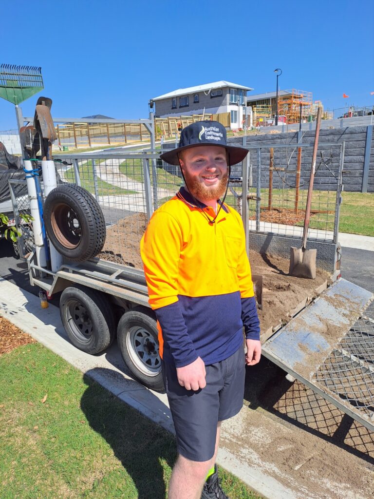 Damian smiling at the camera while working outdoors - taking another step towards his goals through youth employment services.